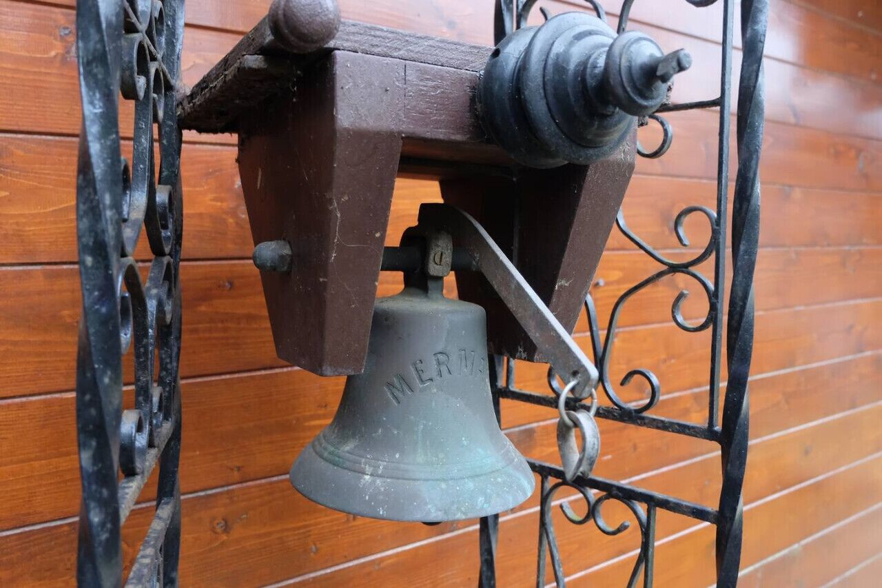 A vintage bell with the inscription "MERRY" mounted on a metal stand with ornate scrollwork.