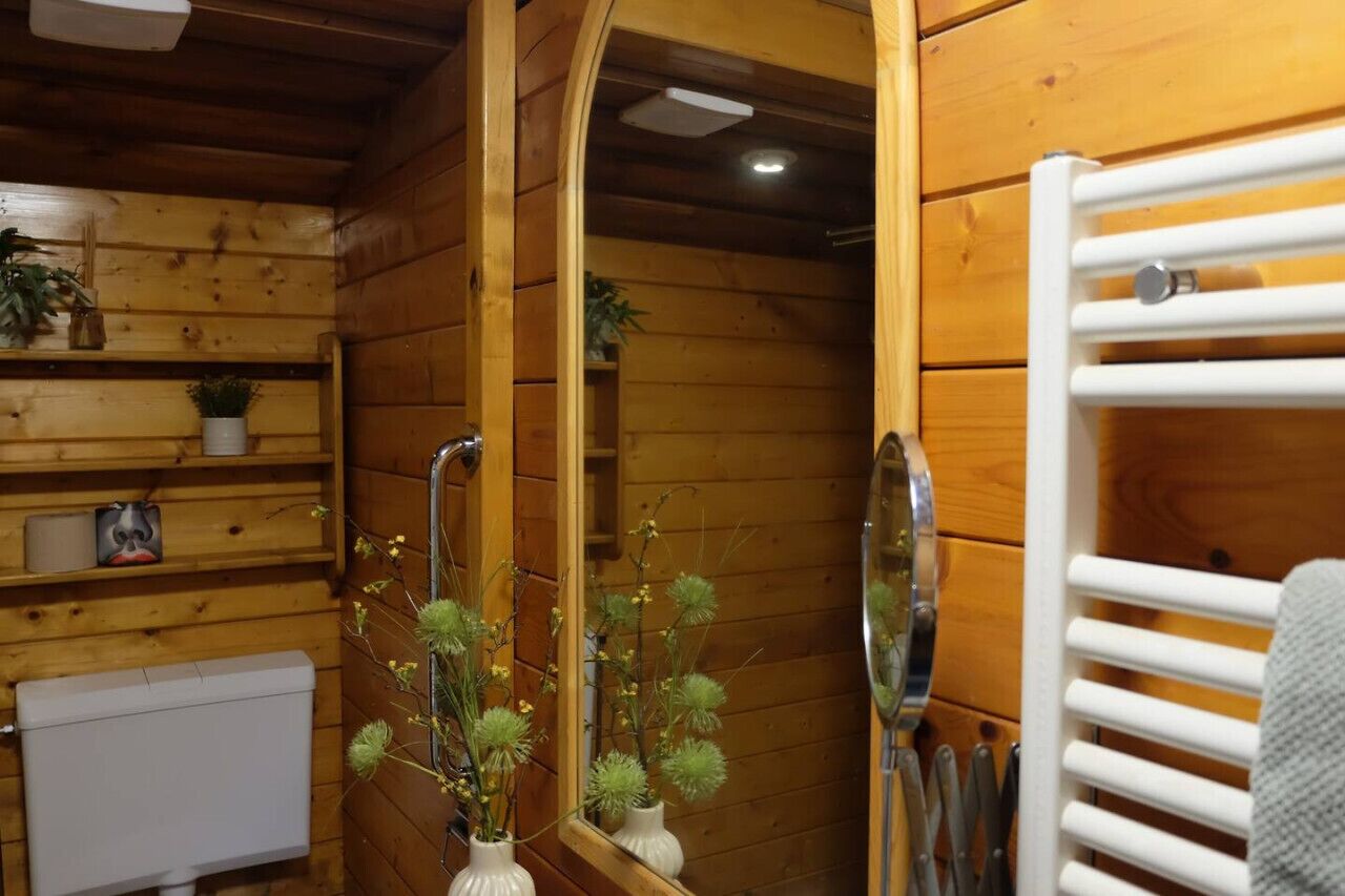 Une salle de bain rustique, avec des murs en bois, un radiateur blanc, un miroir et une étagère contenant des articles de toilette.
