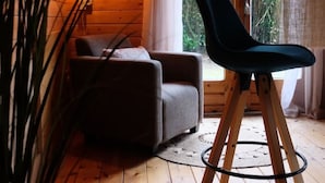A cozy cabin interior with a wooden ceiling, a sofa, a chair, and a large window with curtains.