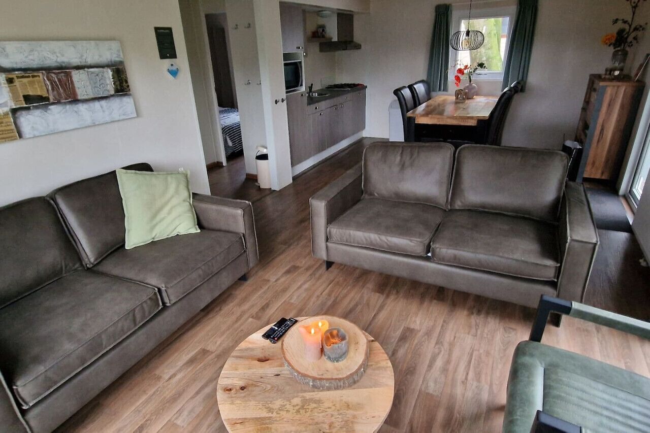 A modern living room with a brown leather sofa, a round coffee table with a candle, and a dining area with a wooden table and chairs.