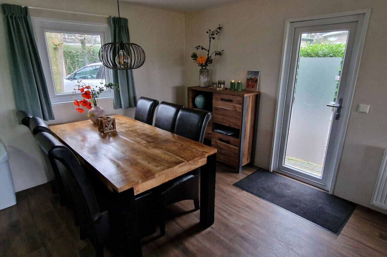 Un coin repas avec une table en bois et des chaises noires, un vase rempli de fleurs et un meuble contenant des objets décoratifs.