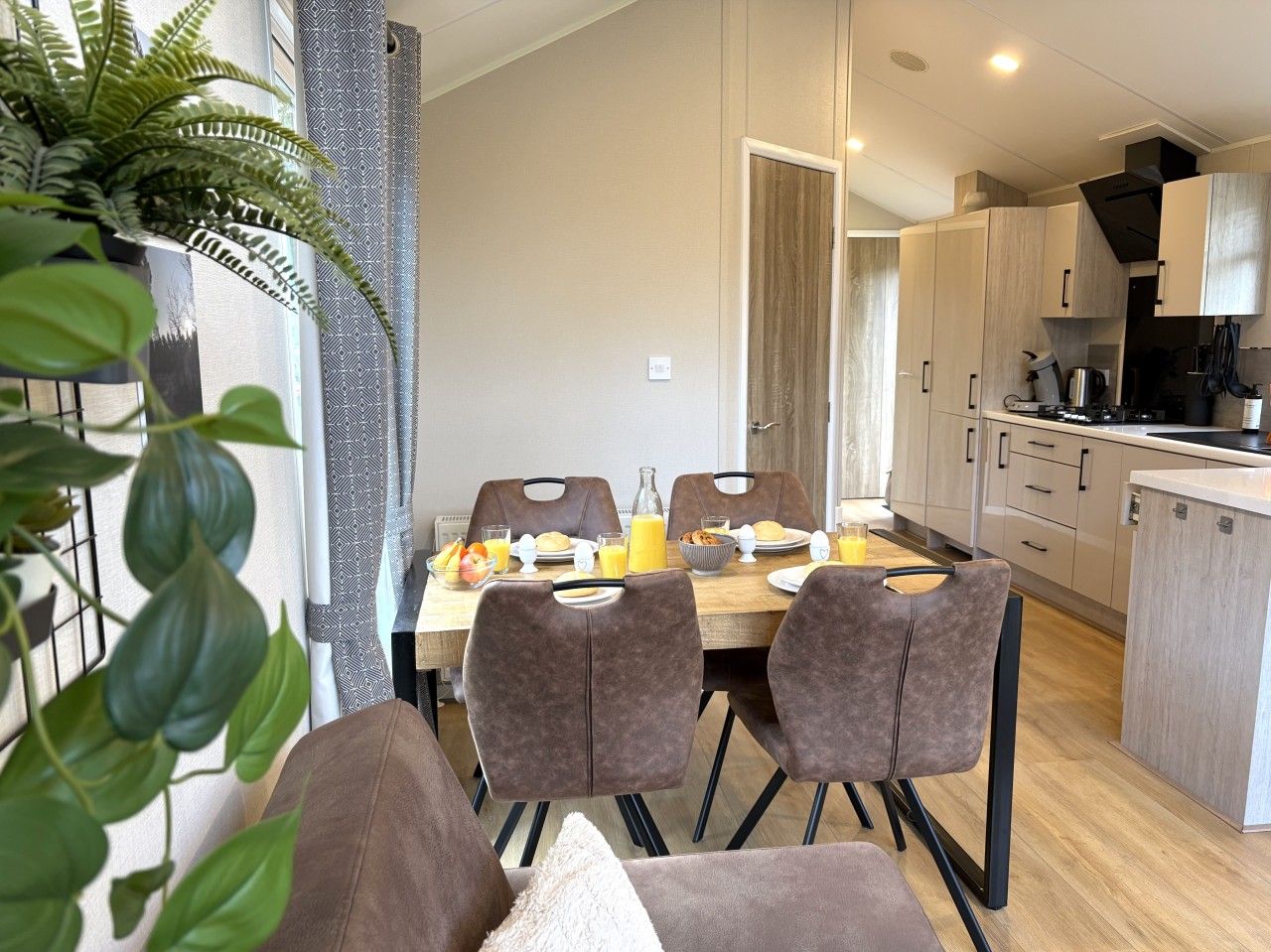 A modern kitchen with a dining area, featuring a table set with plates, glasses, and a fruit bowl.