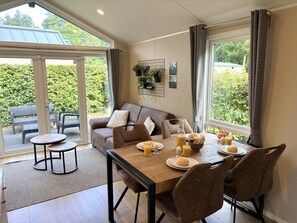 A dining area with a table set for breakfast, a sofa, and a view through a glass door. - Modern chalet met grote tuin, hondvriendelijk | Epe, Veluwe (Epe)