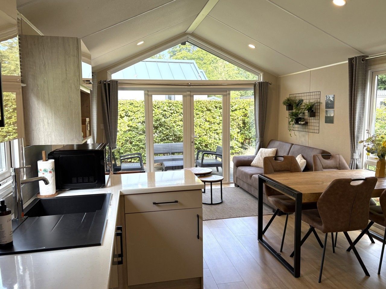 A modern kitchen with a dining area, large windows, and a view of greenery.