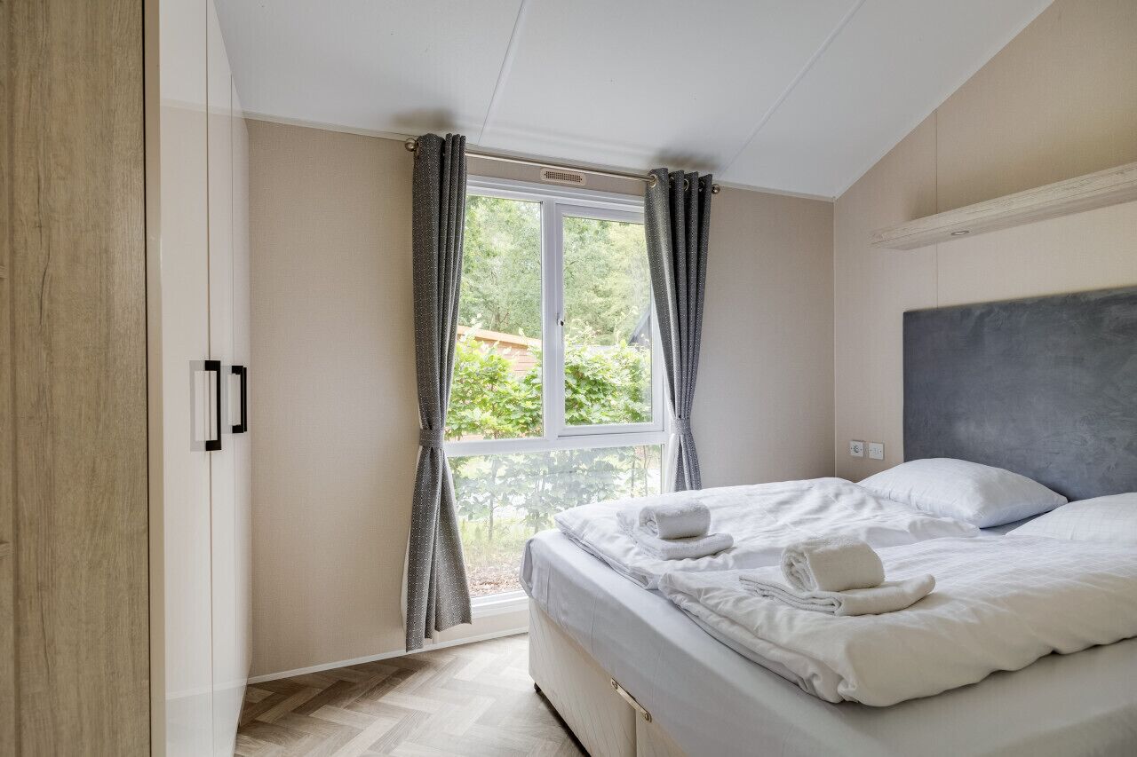 A bedroom with a bed, a window with curtains, a wardrobe, and a headboard.