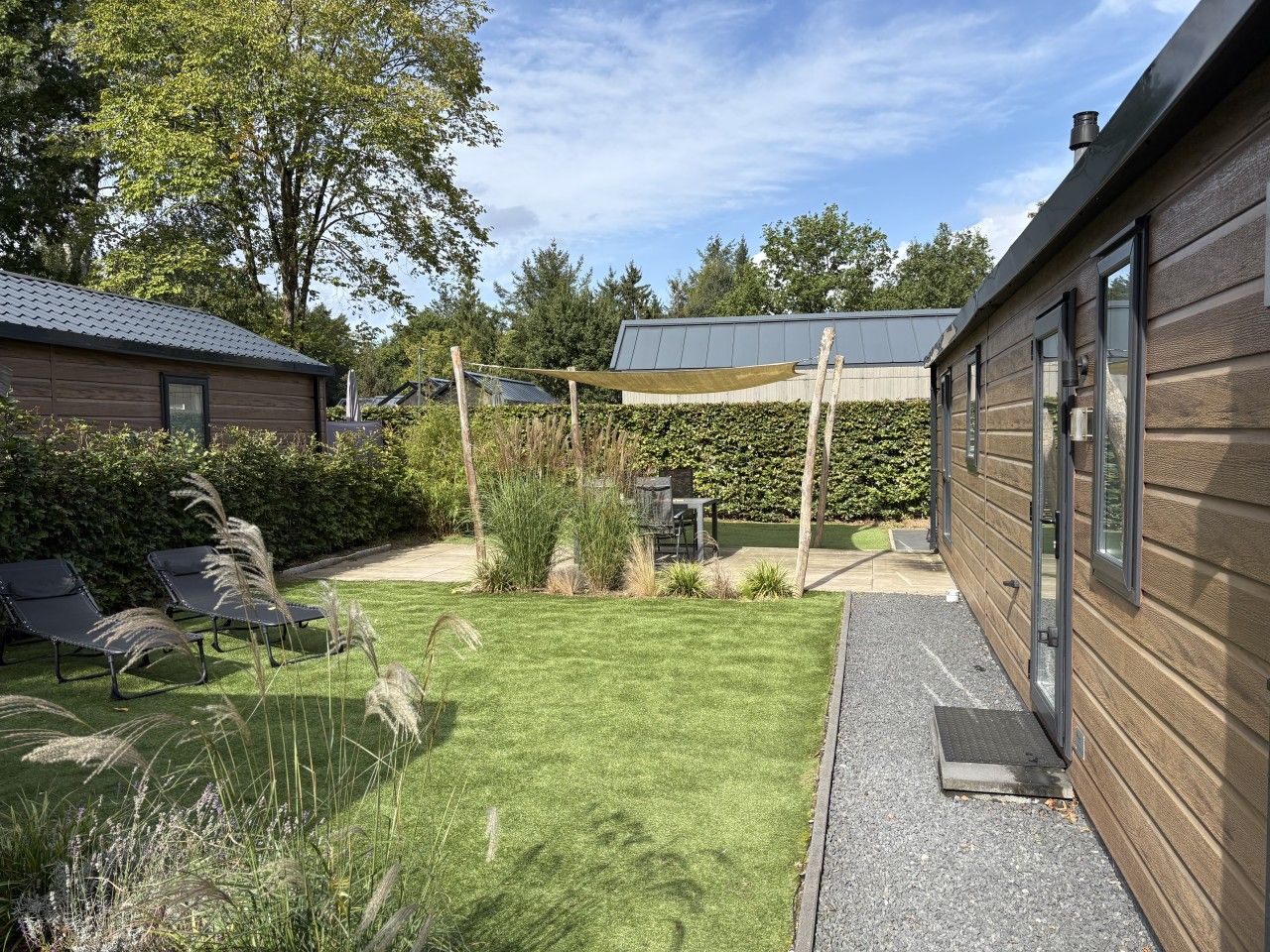 A residential backyard with a lawn, two lounge chairs, a wooden house, and a covered patio area.