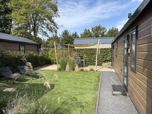 A residential backyard with a lawn, two lounge chairs, a wooden house, and a covered patio area.