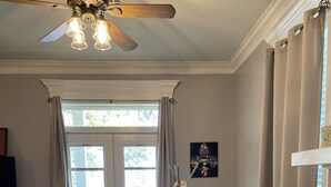 A living room with a wooden floor, a beige sofa, a ceiling fan, and a large window with curtains. - Waterfront Bayou living only 30 minutes from New Orleans, Dock Fishing (Lafitte)