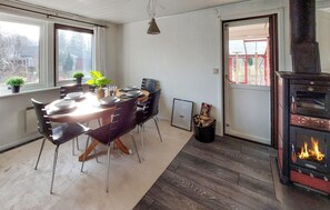 Ruokailutilassa on pyöreä pöytä, mustat tuolit ja ruukussa oleva kasvi. Siellä on myös takka, jossa näkyy tuli, sekä ovi, joka johtaa ulos.