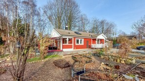 Ein rotes Haus mit Veranda, umgeben von Bäumen und einem Garten mit erhöhten Beeten.