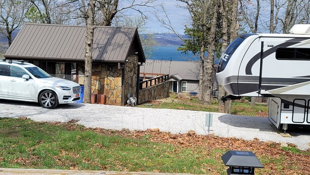 A campsite with a stone building, a white RV, and a white car parked nearby. - Year Around View Lake Tenkiller (Vian)