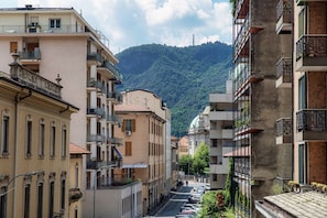 A street lined with multi-story buildings, some with balconies, leading towards a hill with greenery. - Style Suite Apartment - My Home in Como (Como)