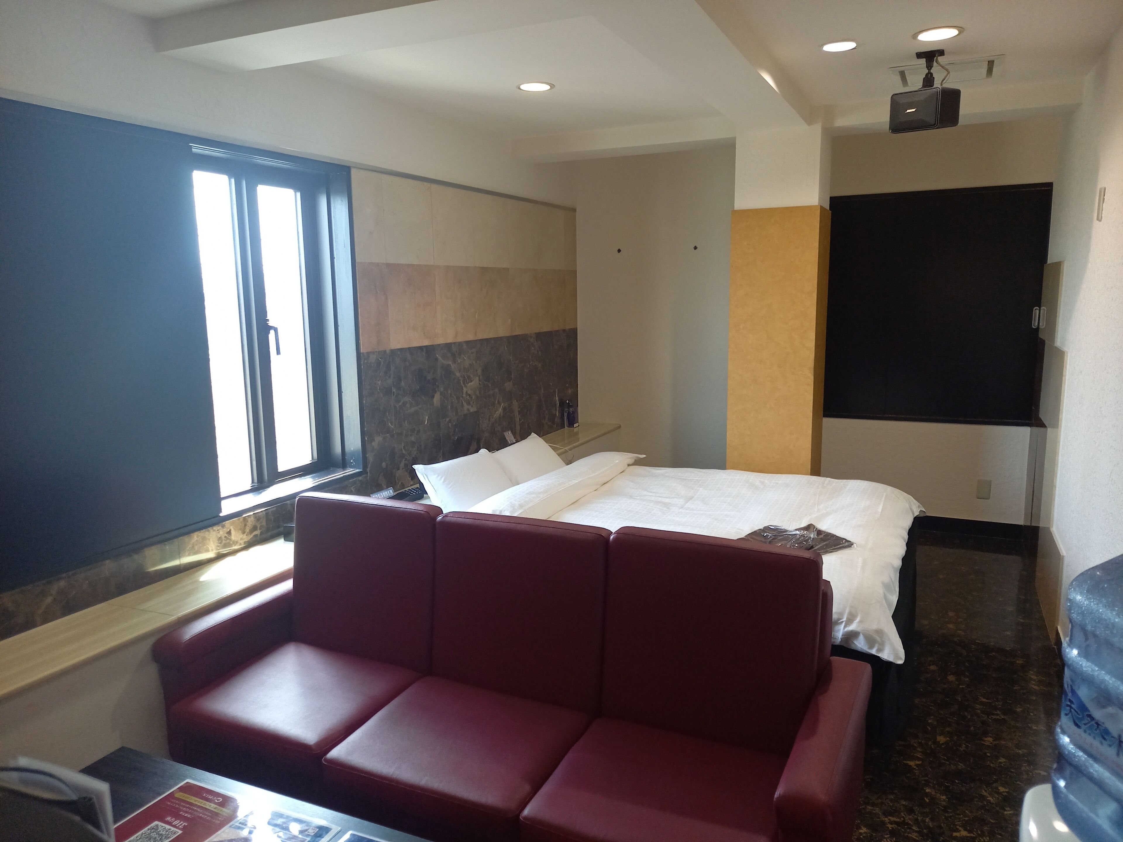 Una habitación de hotel con una cama, un sofá rojo, un ventanal grande y un televisor de pantalla plana.