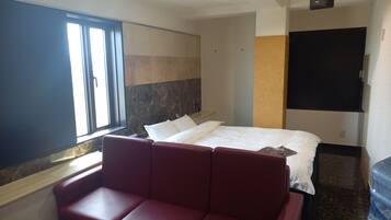 Una habitación de hotel con una cama, un sofá rojo, un ventanal grande y un televisor de pantalla plana.