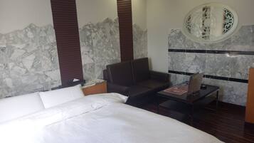 A hotel room with a large bed, a seating area, and a small table with a magazine.