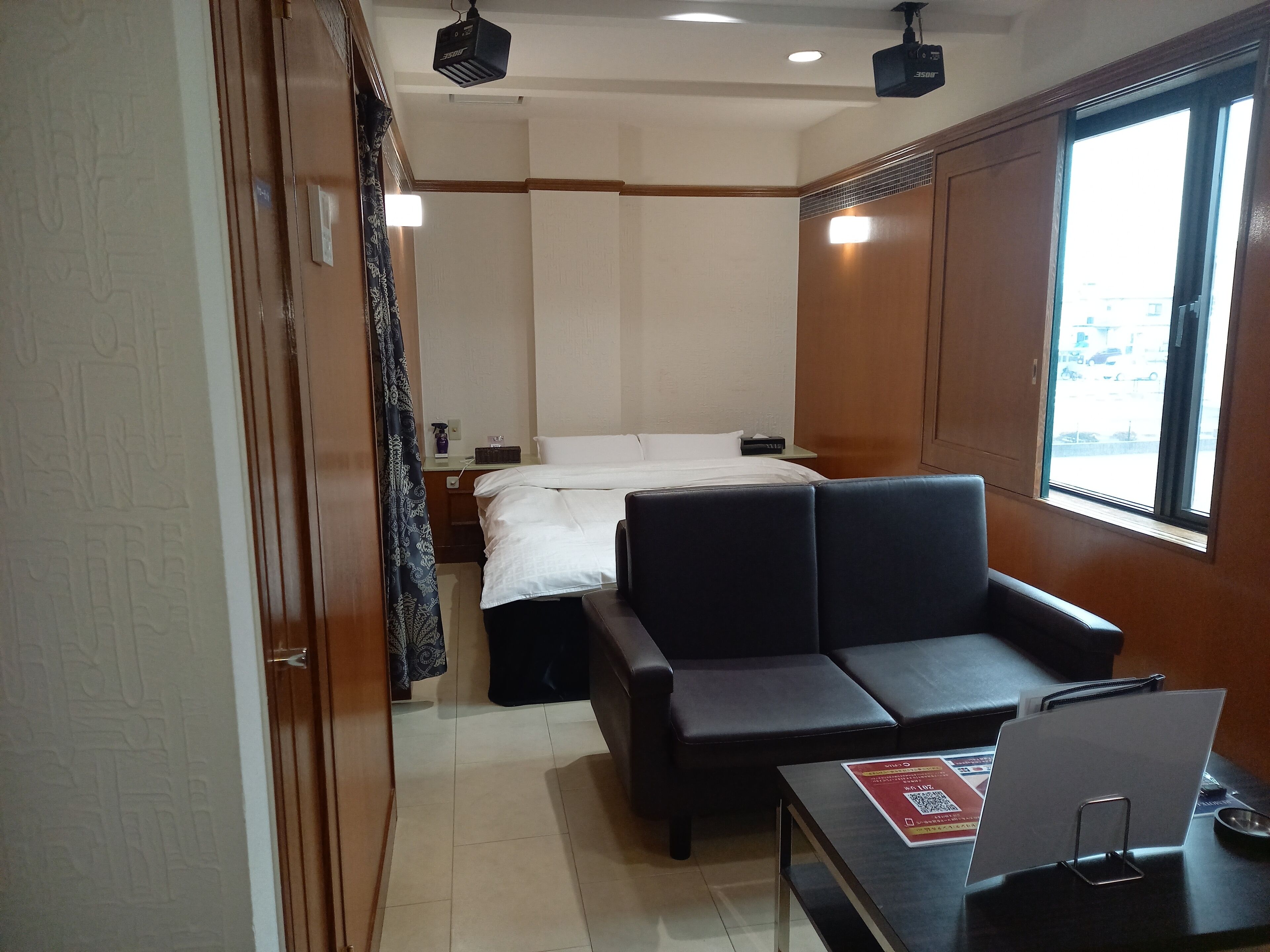 A hotel room with a bed, a sofa, a small table with a sign, and a window with a view.