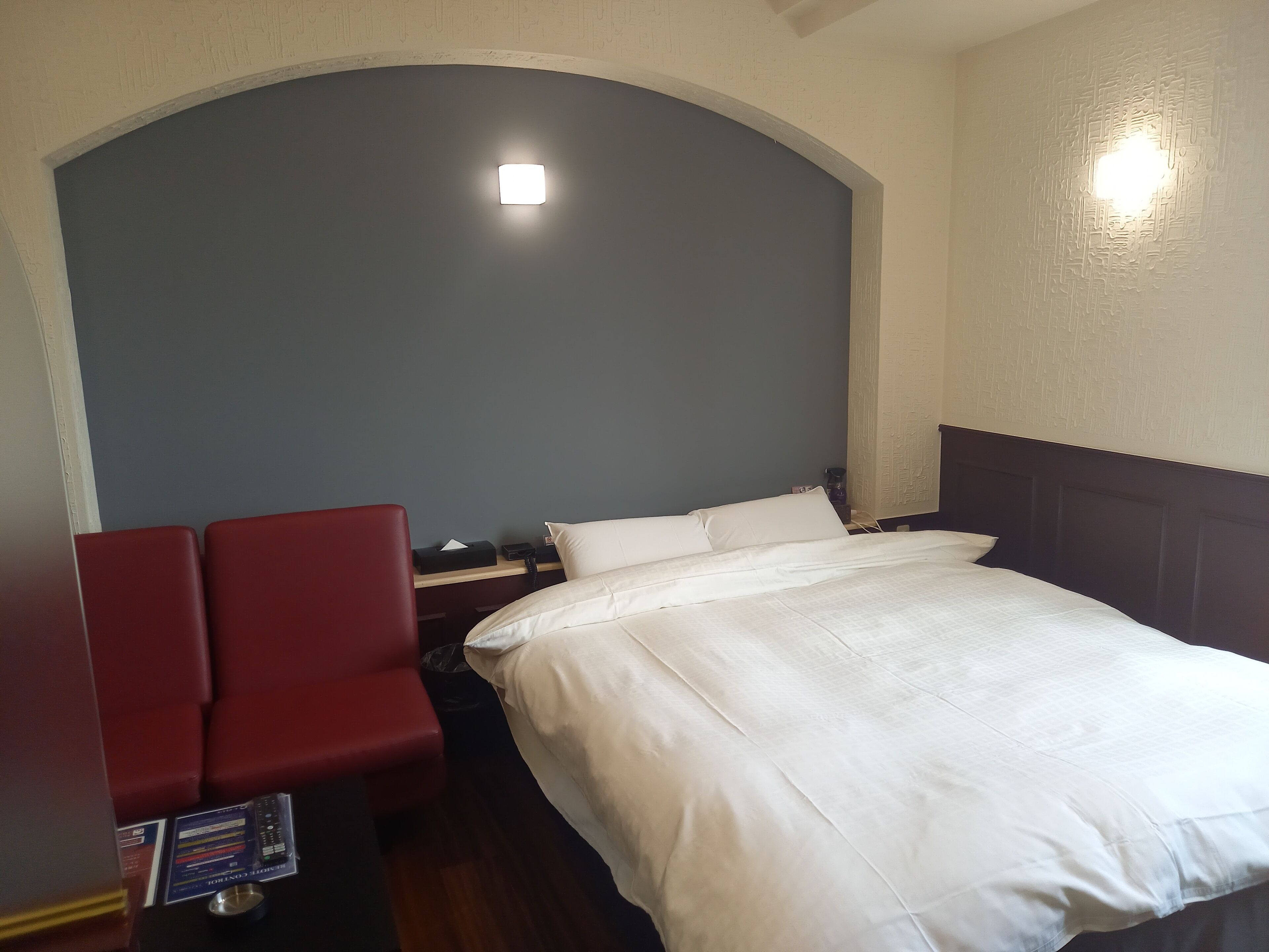 A hotel room with a large bed, a red armchair, a bedside table with a lamp, and a small table with a menu.