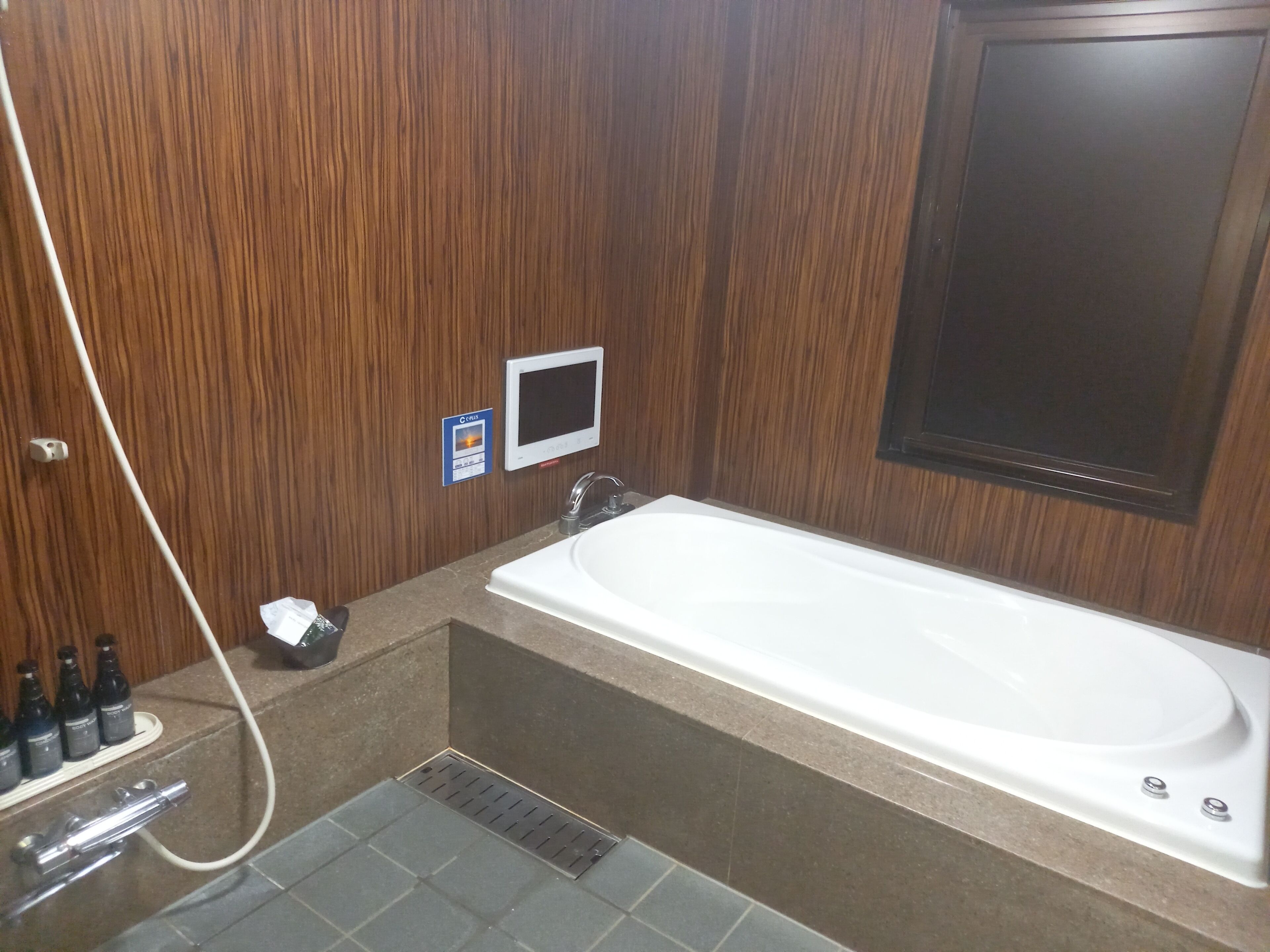 Un baño con pared de madera, una bañera blanca, un lavamanos pequeño y un cabezal de ducha de mano.