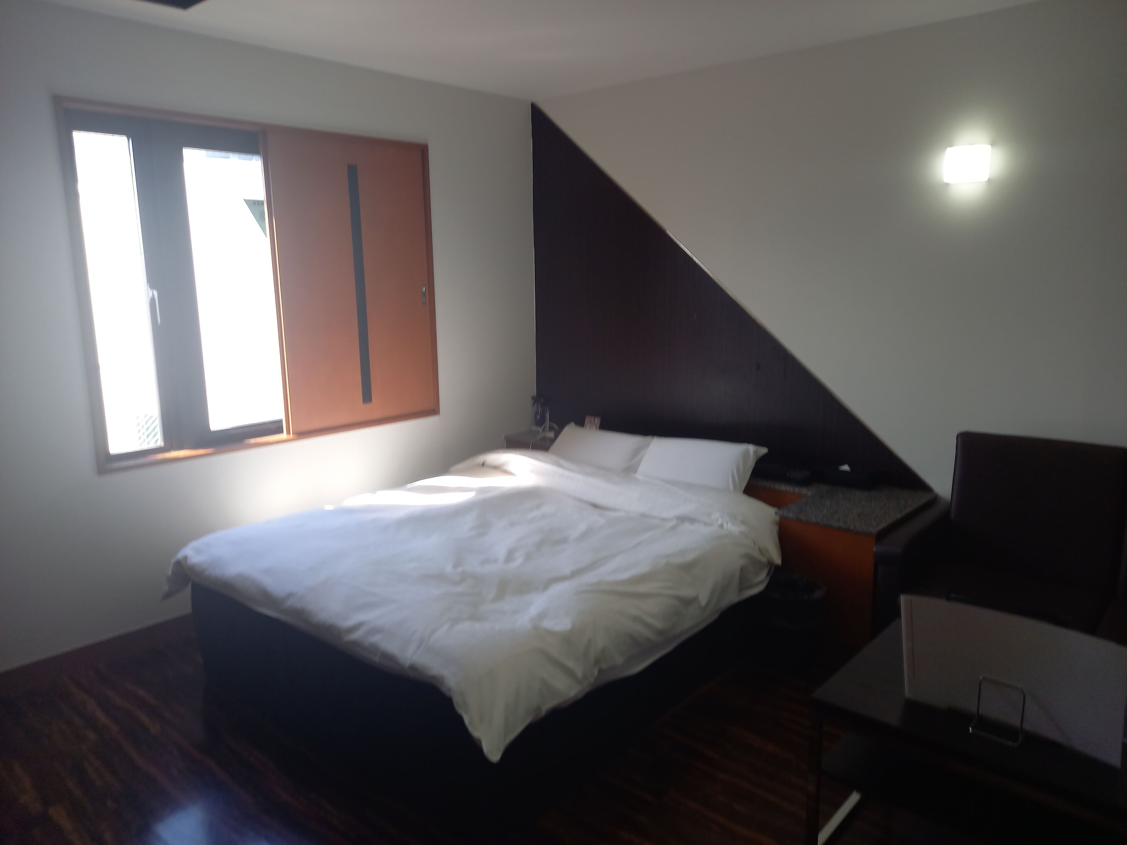 A bedroom with a bed, a nightstand, a desk, and a window.