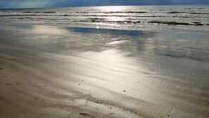 A beach with a wide sandy shore and a view of the ocean under a partly cloudy sky. - "Nomadica"-Modern, Top Floor Beachfront Amazing Views & Beach Access (Galveston)
