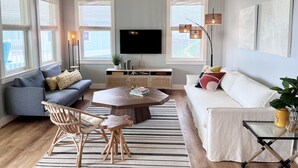 A modern living room with a sofa, a coffee table, a TV, and a ceiling fan. - "Nomadica"-Modern, Top Floor Beachfront Amazing Views & Beach Access (Galveston)