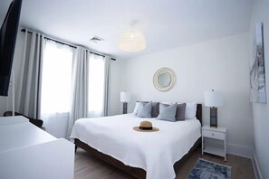 A hotel room with a large bed, a bedside table, a lamp, a hat on the bed, and a window with curtains. - Fully renovated 3 Bedroom 2 bath apartment 1.5 blocks from the beach (Wildwood)
