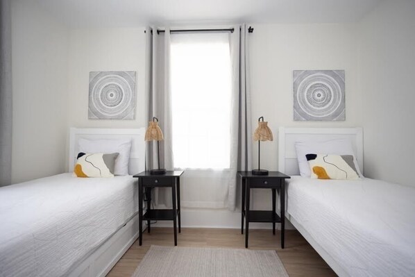 A bedroom with two beds, a window with curtains, and two wall-mounted lamps. - Fully renovated 3 Bedroom 2 bath apartment 1.5 blocks from the beach (Wildwood)