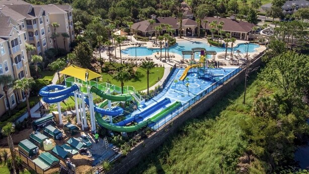 Ein Wasserpark mit mehreren Pools und Wasserrutschen, umgeben von Gebäuden und Grünflächen.