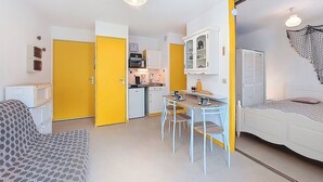 Ett kompakt bostadsutrymme med ett litet kök, en matplats och en säng.