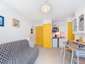Um espaço compacto com sofá, mesa de jantar, cozinha equipada e um relógio na parede.