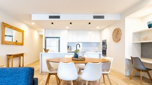 A modern kitchen with white cabinets, a central island, and a dining area with white chairs.