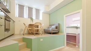 A compact living space with a kitchenette, a dining area with chairs, a sofa, and a bed. - GuestHost - Insubria Park - Pastel Colored Apartment! (Milano)