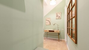 A hallway with a desk, a lamp, and artwork on the wall. - GuestHost - Insubria Park - Pastel Colored Apartment! (Milano)