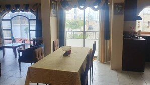 Un comedor con mesa y sillas, una zona de cocina y ventanas grandes con cortinas.