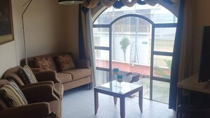Una sala de estar con un sofá, una mesa de centro de vidrio y un ventanal con vistas al exterior.