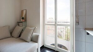 A room with a bed, a window with a view of buildings, a small table with a plant, and a wall-mounted light switch. - GuestHost - Corvetto M3 - Comfortable Apt. with balcony! (Milano)