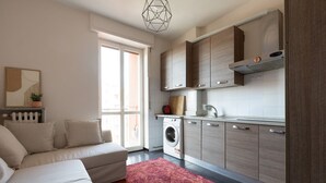 A modern kitchen with a washing machine, wooden cabinets, and a large window. - GuestHost - Corvetto M3 - Comfortable Apt. with balcony! (Milano)