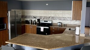 Cozinha moderna com bancadas de granito, eletrodomésticos de aço inoxidável e uma ilha central com banquetas.
