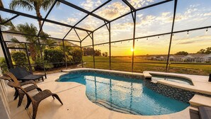Une piscine à bords incurvés, entourée d’une terrasse couverte aménagée avec des chaises et offrant une vue sur le coucher de soleil.