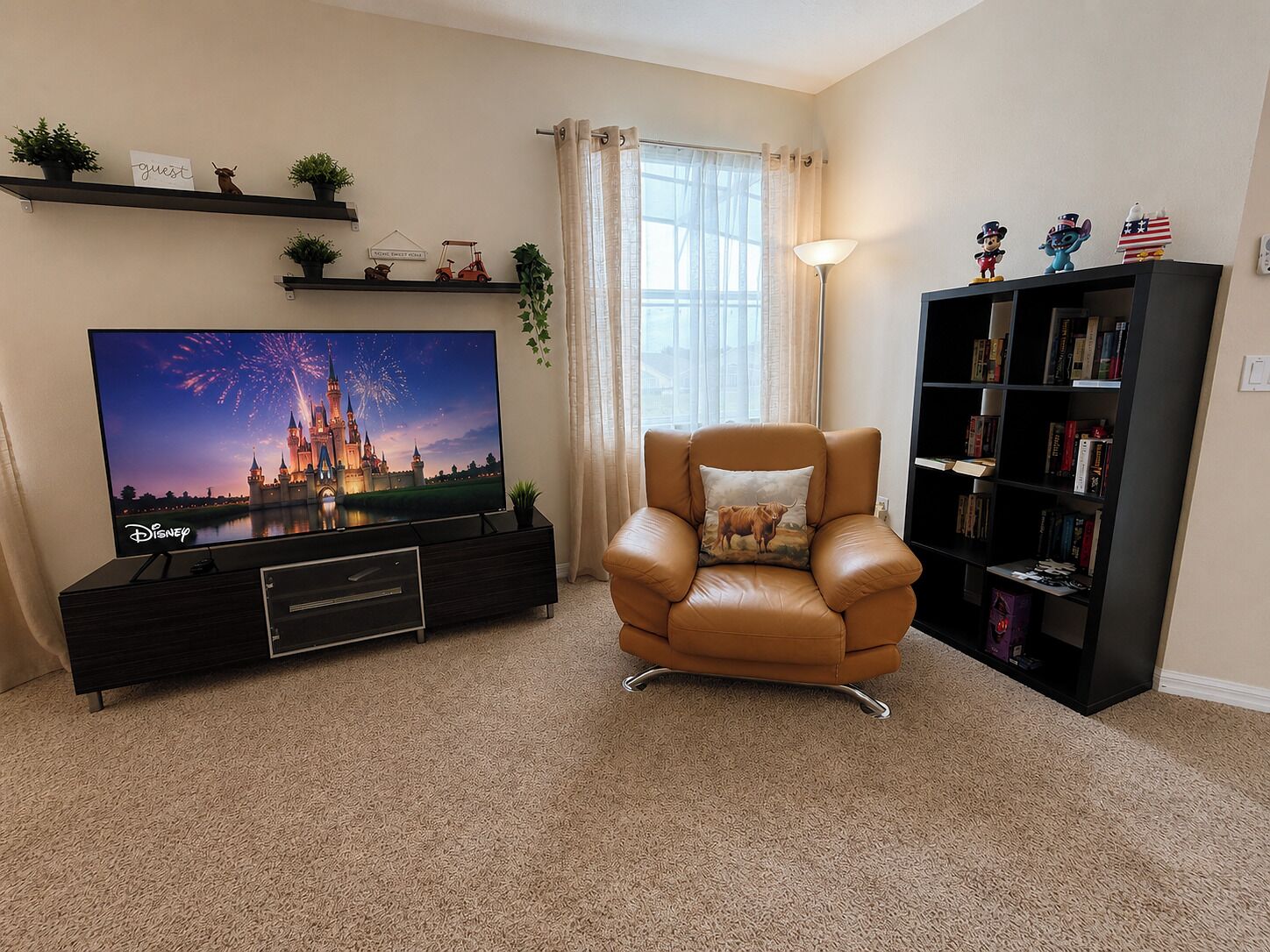 A living room with a flat-screen TV displaying fireworks, a leather armchair, a bookshelf, and a 'guest' sign on the wall.
