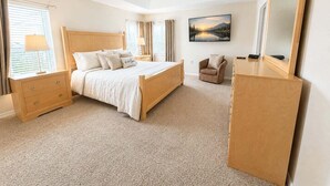 Une chambre à coucher comprenant un lit, une table de chevet, une chaise, une commode, un ventilateur de plafond et un tableau accroché au mur.