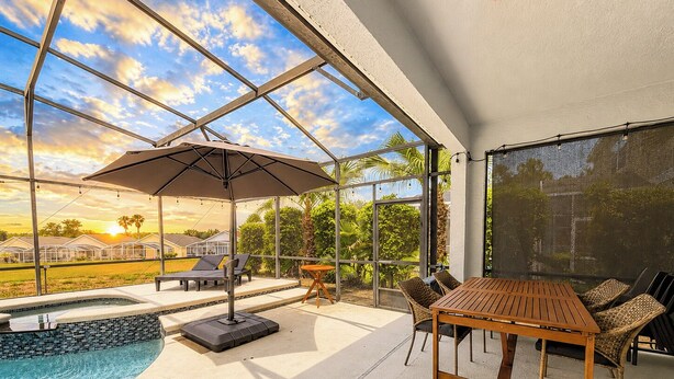 Un espace aménagé au bord de la piscine, avec une table et des chaises, un parasol et une vue sur un quartier résidentiel.