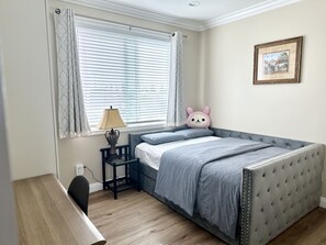 A bedroom with a bed, a desk, a chair, a lamp, a picture frame, and a window with blinds.