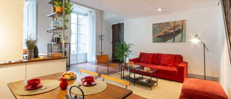 A modern living room with a red sofa, a coffee table, and a dining area with a wooden table and chairs.