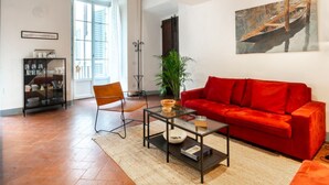 A living room with a red sofa, a glass coffee table, a chair, a plant, and a painting on the wall.
