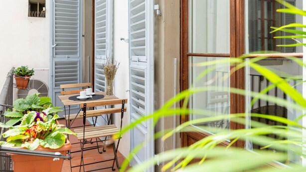 A balcony with a table, chairs, potted plants, and a sliding glass door.