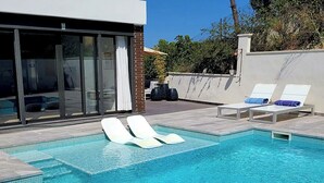 A modern outdoor pool area with lounge chairs and a glass-enclosed patio. - Villa with beautiful swimming pool  (CT)