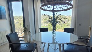A modern dining area with a glass table and black chairs, a decorative plant, and a view of a hilly landscape through large windows. - Villa with beautiful swimming pool  (CT)
