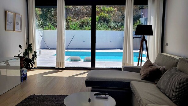 A modern living room with a sofa, a coffee table, and a view of a swimming pool through large sliding doors. - Villa with beautiful swimming pool  (CT)