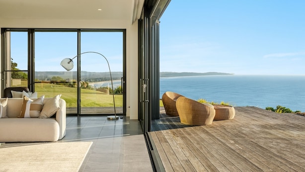 Una sala de estar moderna con un amplio ventanal que da a una terraza de madera con vista al mar.